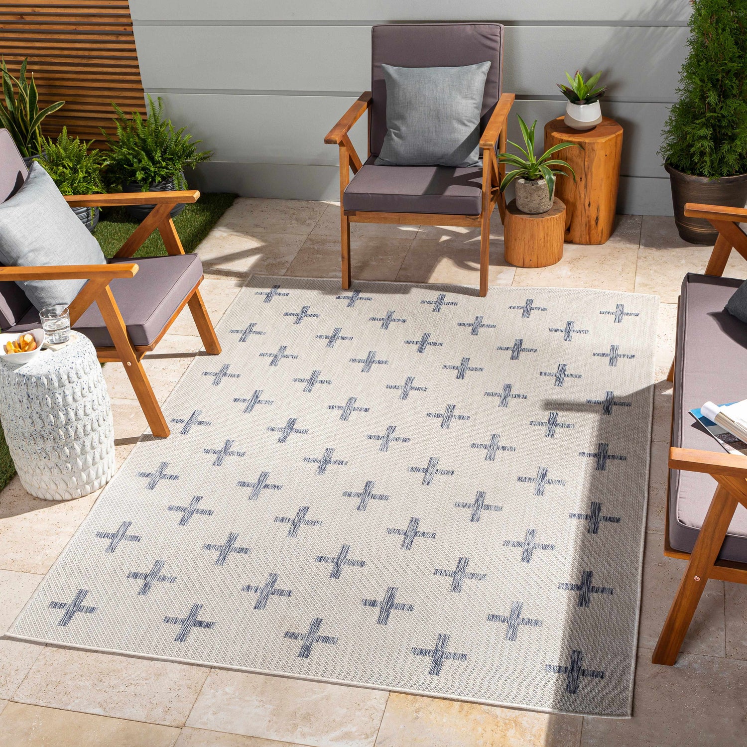 Outdoor patio scene with Pangao Area Rug in cream and navy, geometric pattern, surrounded by wooden chairs and potted plants. Roomscene-Rectangle
