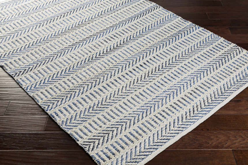 Close-up of Pontian Area Rug: Beige jute rug with blue and black chevron pattern on dark wood floor. Corner