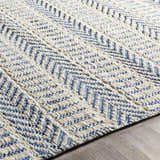 Close-up of the hand woven Pontian Area Rug. Beige jute rug with a blue herringbone pattern. Coastal farmhouse style. Texture