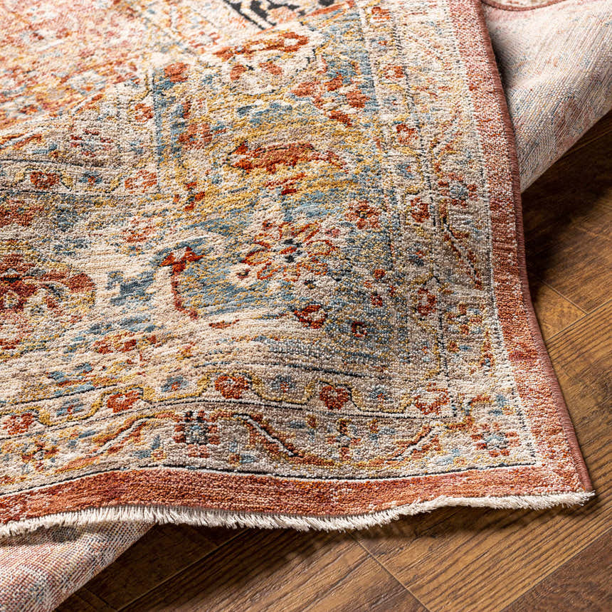 Close-up of the Polomolok Luxe Performance Rug. Traditional oriental pattern with brick red, cream, and blue accents on wood floor. Fold