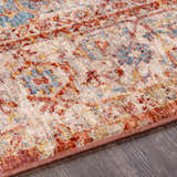 Close-up of the Powassan Area Rug showing its brick red, teal, and beige traditional pattern and soft texture. Texture