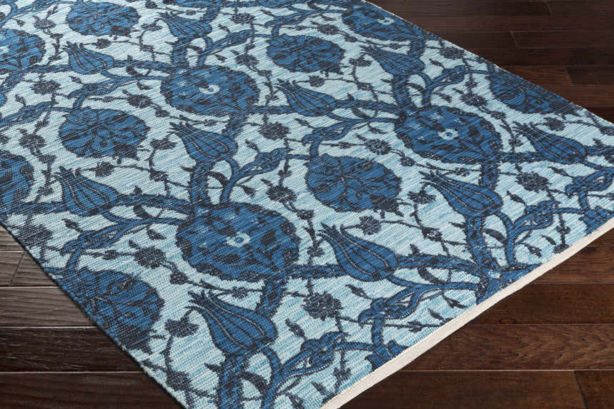 Close-up of the Premier Area Rug Clearance, a hand-woven cotton rug with a blue floral pattern on dark wood flooring. Corner