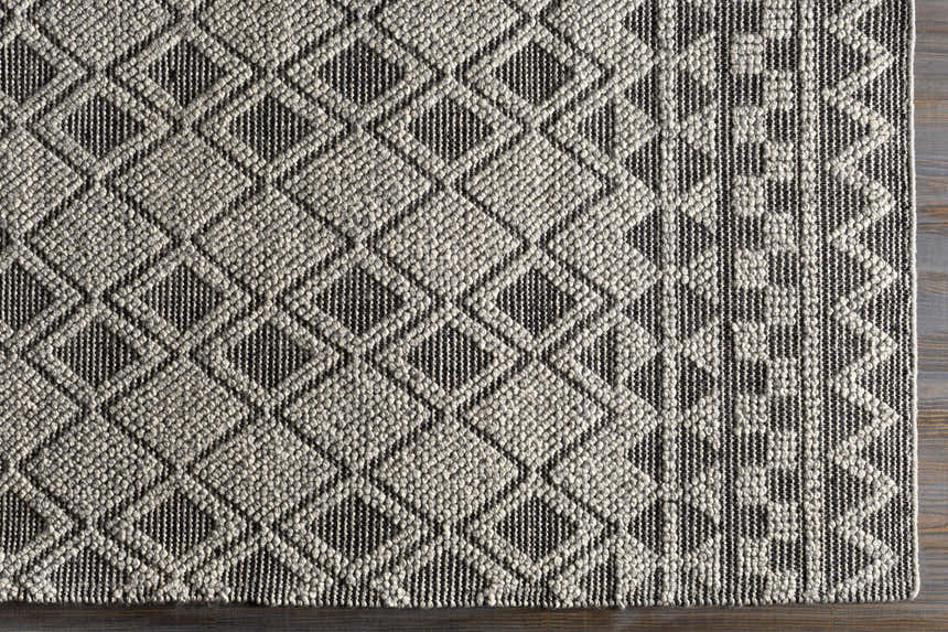 Close-up of the hand woven Post Area Rug. Features a geometric diamond pattern in neutral gray and black tones. Swatch