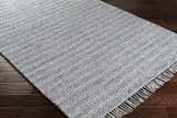 Close-up of the Potterspury Area Rug. Hand-loomed rug in blue, cream, and gray on a dark wood floor. Contemporary style. Corner