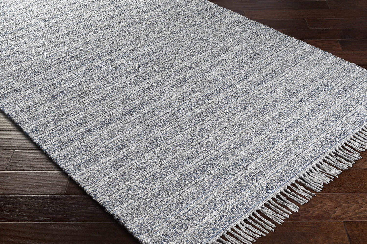 Close-up of the Potterspury Area Rug. Hand-loomed rug in blue, cream, and gray on a dark wood floor. Contemporary style. Corner
