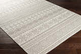 Close-up of the Pumwani Area Carpet. Cream and gray wool rug with a geometric, bohemian-inspired pattern. Hand woven texture. Corner