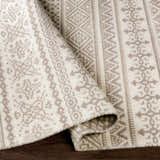 Close-up of the hand-woven Pumwani Area Carpet. Cream wool rug with gray bohemian-style pattern and fringe detail. Fold