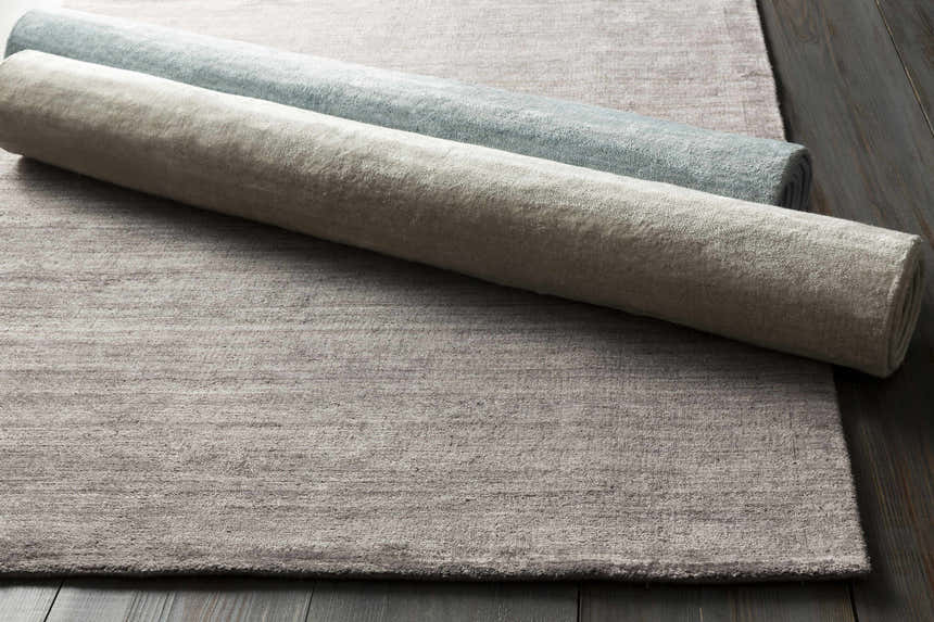 Close-up of the textured Barree Area Carpet, a white hand-loomed viscose rug, rolled and ready for a bathroom, kitchen, or mudroom. Styleshot