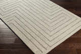 Close-up of the Queenton Area Rug, a light gray wool rug with a charcoal geometric pattern on a dark wood floor. Corner