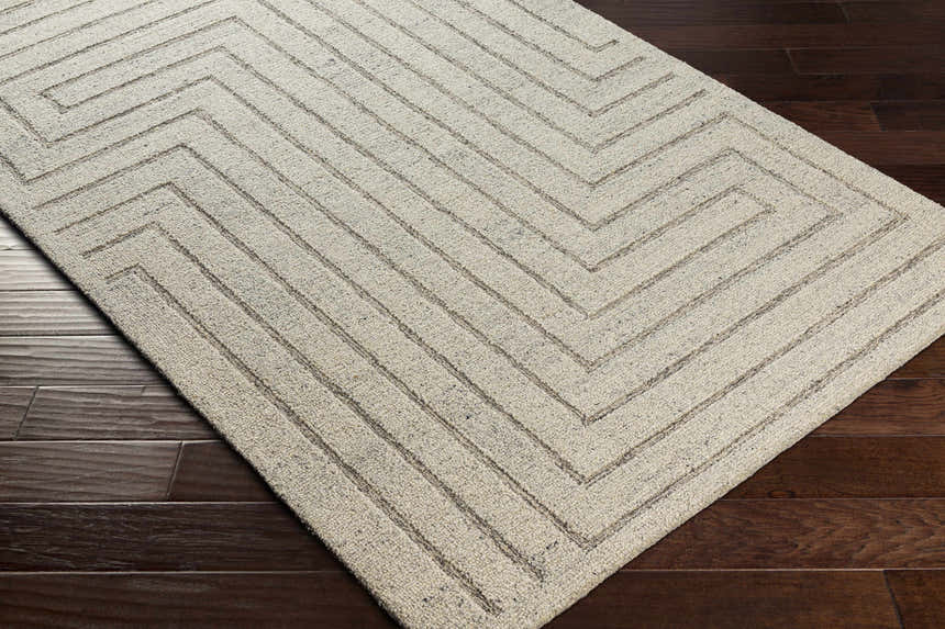 Close-up of the Queenton Area Rug, a light gray wool rug with a charcoal geometric pattern on a dark wood floor. Corner