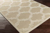 Close-up of the neutral Quicksand Area Rug showing the quatrefoil pattern and hand-tufted texture on dark wood floors. Corner