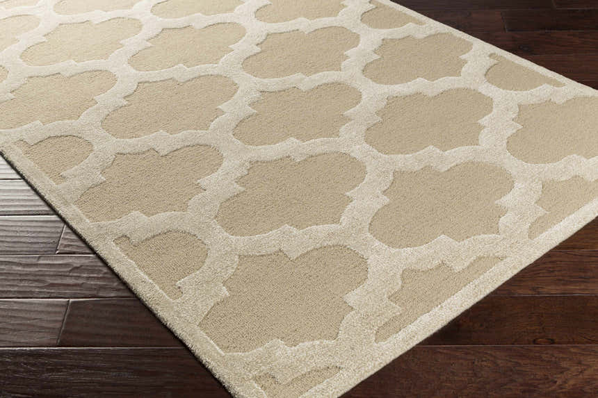 Close-up of the neutral Quicksand Area Rug showing the quatrefoil pattern and hand-tufted texture on dark wood floors. Corner