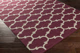Close-up of the Racine Area Carpet. Dark purple cotton rug with an ivory quatrefoil pattern on a dark wood floor. Corner