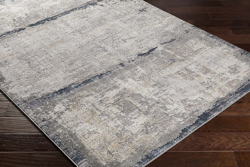 Close-up of Rainworth Modern Slate Luxe Rug showing charcoal, beige, and gray abstract pattern on dark wood floor. Corner