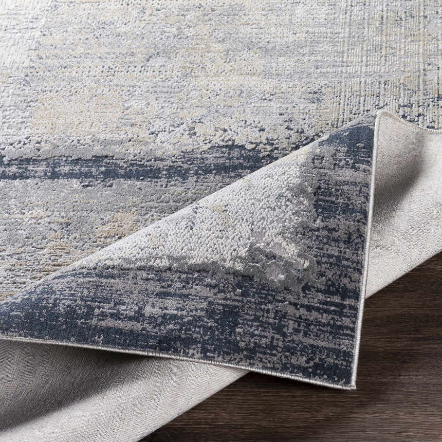 Close-up of the Rainworth Modern Slate Luxe Rug showing charcoal, beige, and gray tones and machine-woven texture. Fold