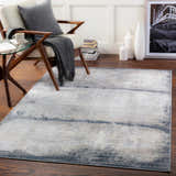 Living room scene with a Rainworth Modern Slate Luxe Rug, chair, glass table, and wood floors. Roomscene-Rectangle