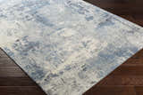 Close up of the Ramsbottom Area Rug on dark wood floors. Contemporary style rug in cream, blue, and charcoal. Corner