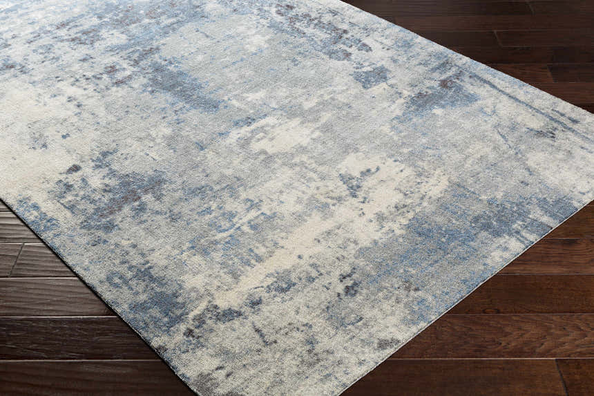 Close up of the Ramsbottom Area Rug on dark wood floors. Contemporary style rug in cream, blue, and charcoal. Corner