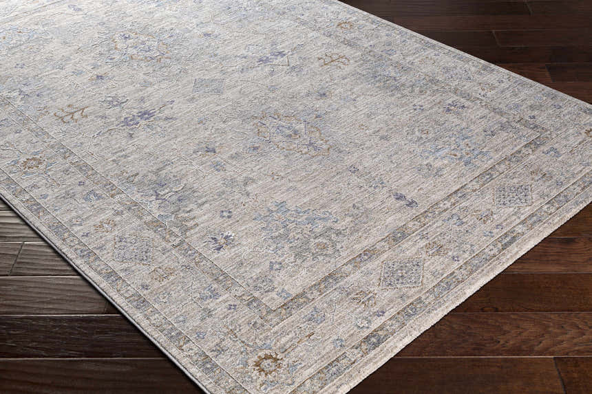 Close-up of Rochedale Area Rug. Cream rug with traditional lavender and olive floral pattern on dark wood floor. Corner