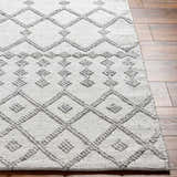 Close-up of the Rick Area Rug, a hand-woven rug with a geometric diamond pattern in arctic stone and gray tones. Front