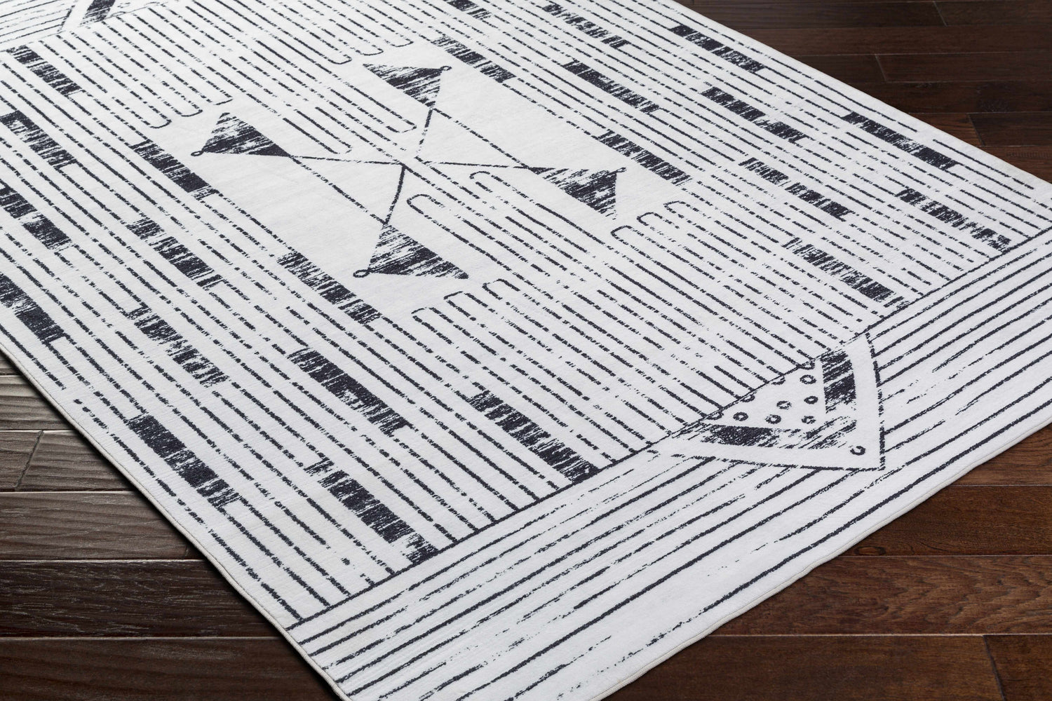 Close-up of the Regis Washable Area Rug. Farmhouse style rug with gray, light silver, and white geometric pattern. Corner