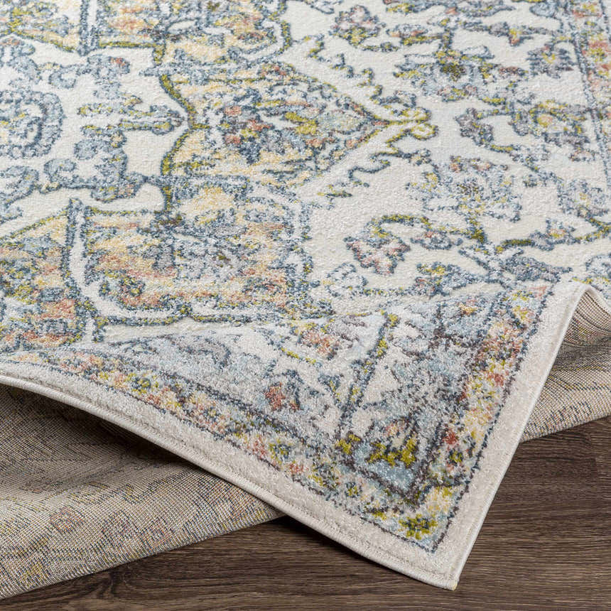 Close-up of Reubens Area Rug showing its ivory, blue, yellow, and coral traditional pattern and machine woven texture. Fold