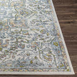 Close up of Reubens Area Rug showing its traditional floral pattern in ivory, blue, yellow and peach on a dark wood floor. Front