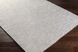 Close-up of Revillo Area Rug on dark wood floor. Light sage, medium gray, tan, teal, and white woven polypropylene rug. Corner