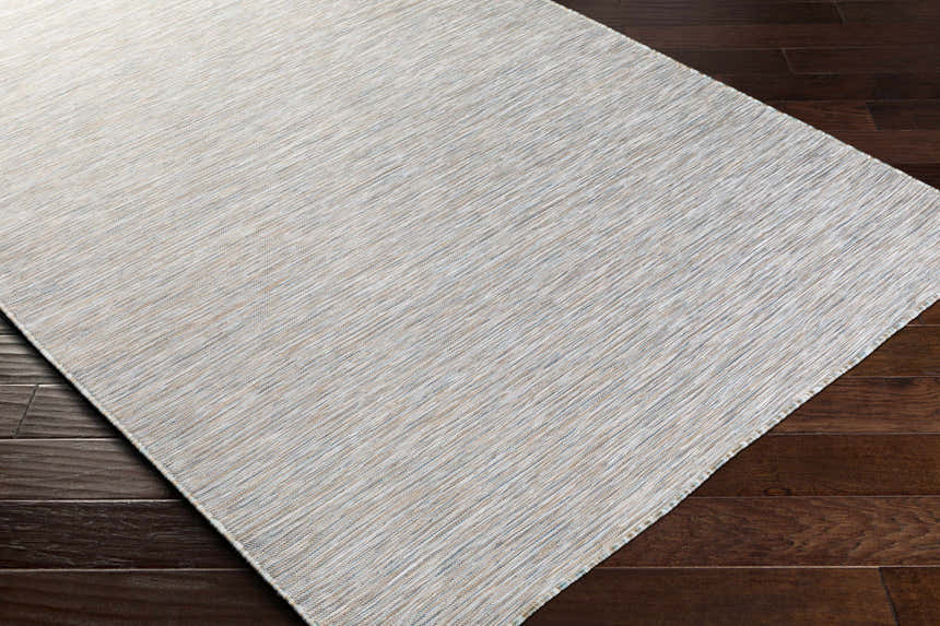 Close-up of Revillo Area Rug on dark wood floor. Light sage, medium gray, tan, teal, and white woven polypropylene rug. Corner