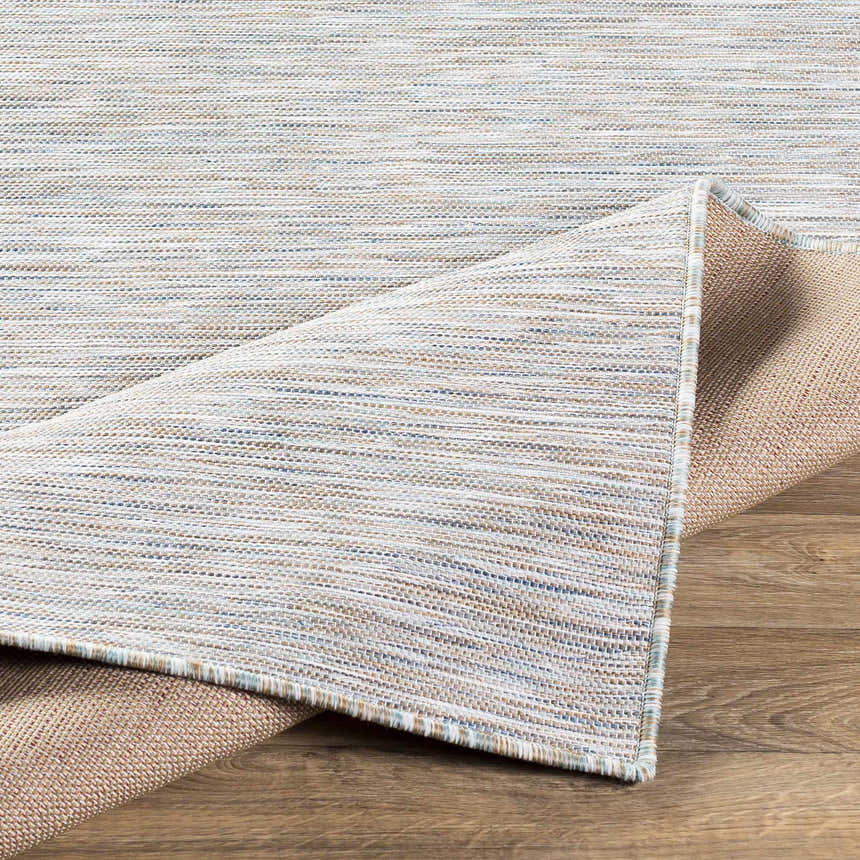 Close-up of the Revillo Area Rug showing its light sage, gray, tan, teal, and white woven texture and backing. Fold
