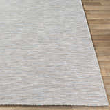 Close-up of the Revillo Area Rug, featuring a woven texture in light sage, tan, gray, teal, and white on a wood floor. Front