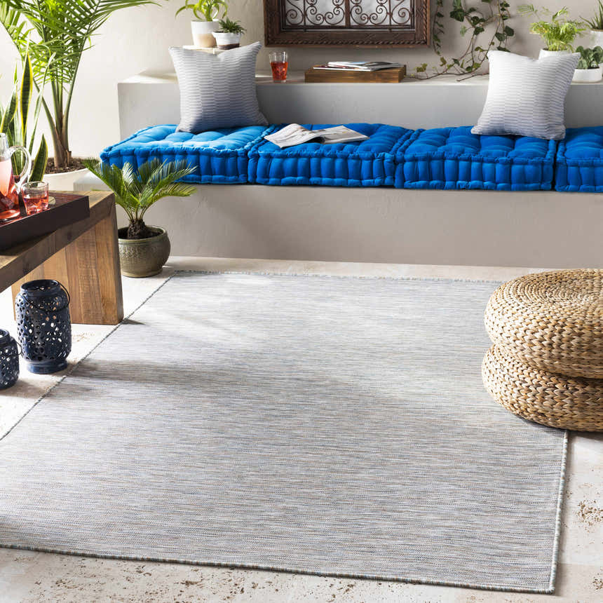 Relaxing patio scene with a light sage Revillo Area Rug, blue cushions, and natural fiber poufs. Roomscene-Rectangle