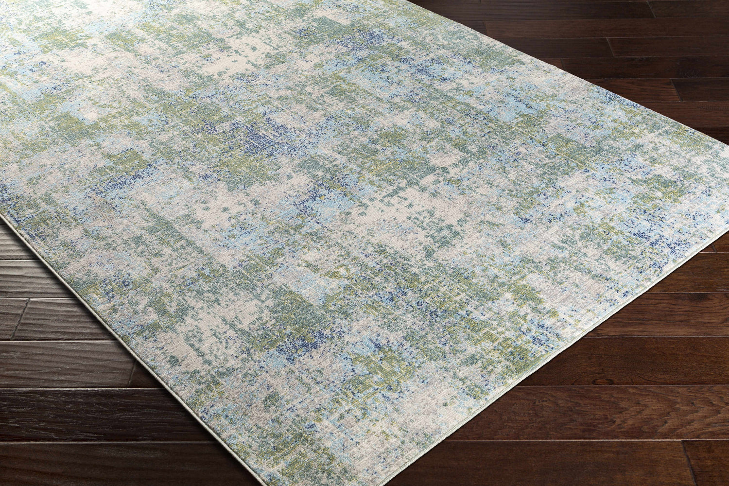 Close-up of the Riegelwood Area Rug. Light beige rug with medium gray, green, navy, and blue abstract pattern. Corner