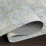 Close-up of the Riegelwood Area Rug showing its light beige, green, and blue coastal-inspired pattern and durable machine-woven construction. Fold