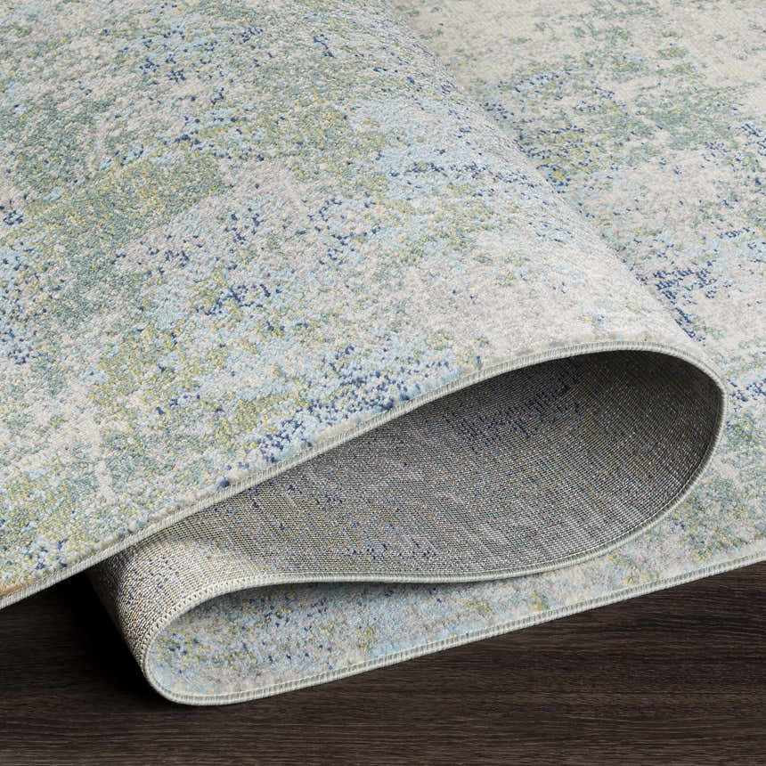 Close-up of the Riegelwood Area Rug showing its light beige, green, and blue coastal-inspired pattern and durable machine-woven construction. Fold