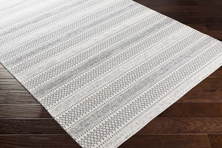 Close-up of Ringtown Washable Area Rug in charcoal and ivory with a geometric, striped pattern on dark wood floors. Corner
