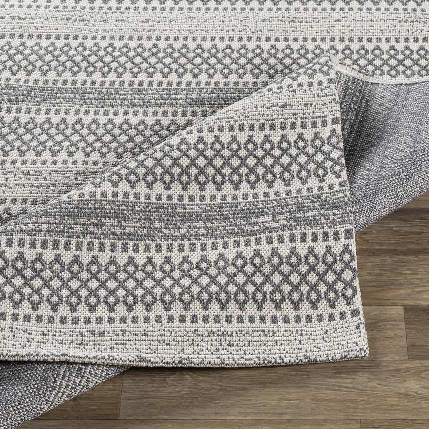 Close-up of the Ringtown Washable Area Rug in charcoal and ivory. Features a geometric, woven pattern and cotton texture. Fold