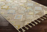 Close-up of Rippon Area Carpet. Hand-woven wool rug with beige, blue, tan, and yellow geometric pattern and tassels. Corner