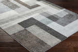 Close-up of Raisa Area Rug featuring a contemporary geometric pattern in aqua, black, cream, and gray tones on dark wood flooring. Corner