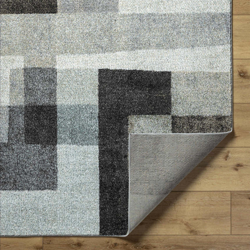 Close-up of Raisa Area Rug showing geometric pattern in aqua, black, cream, and gray on wood floor. Machine woven texture detail. Fold