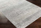 Close-up of the Rombauer Area Rug showing its contemporary gray, off-white, and mustard geometric pattern and texture. Corner