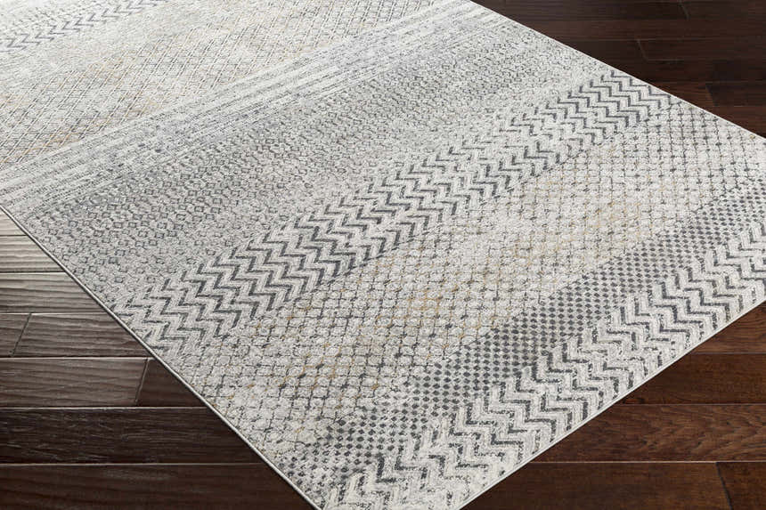 Close-up of the Rombauer Area Rug showing its contemporary gray, off-white, and mustard geometric pattern and texture. Corner
