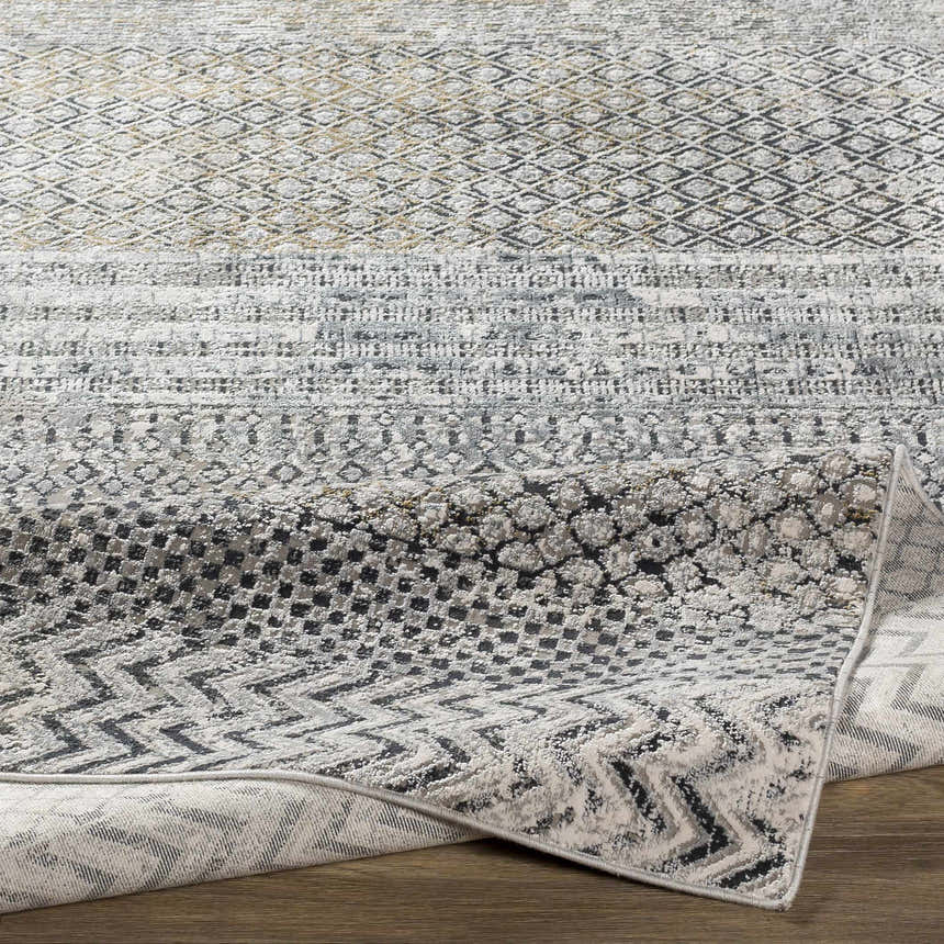 Close-up of the Rombauer Area Rug, showcasing its charcoal, gray, and off-white contemporary pattern and machine-woven texture. Fold
