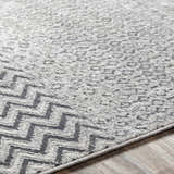 Close-up of the Rombauer Area Rug showing charcoal zigzags and light gray textured pattern on a wood floor. Texture