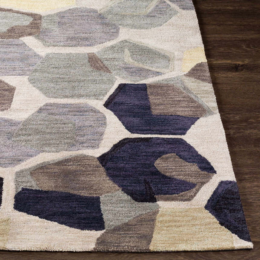 Close-up of the Romoland Area Rug showing a geometric pattern in black, brown, gray, olive, and beige on a dark wood floor. Front