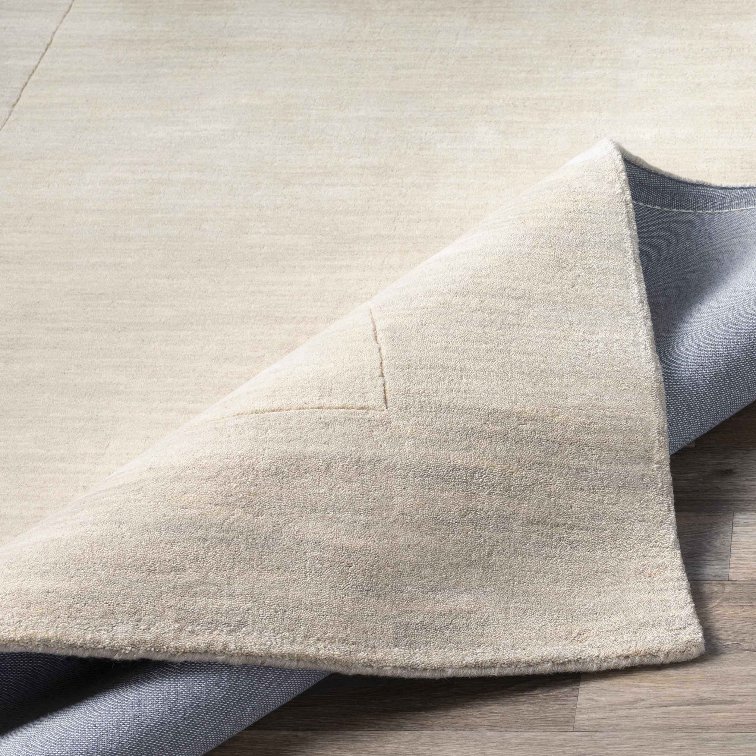 Folded section of Bordered Solid Beige Cream Wool Rug, displaying material thickness and weave. Contemporary Area Rug Backing Canvas 