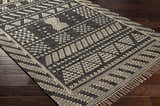 Close-up of the hand woven Rossville Area Rug. Black rug with off-white geometric patterns and fringe. Corner