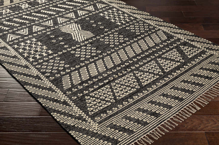 Close-up of the hand woven Rossville Area Rug. Black rug with off-white geometric patterns and fringe. Corner