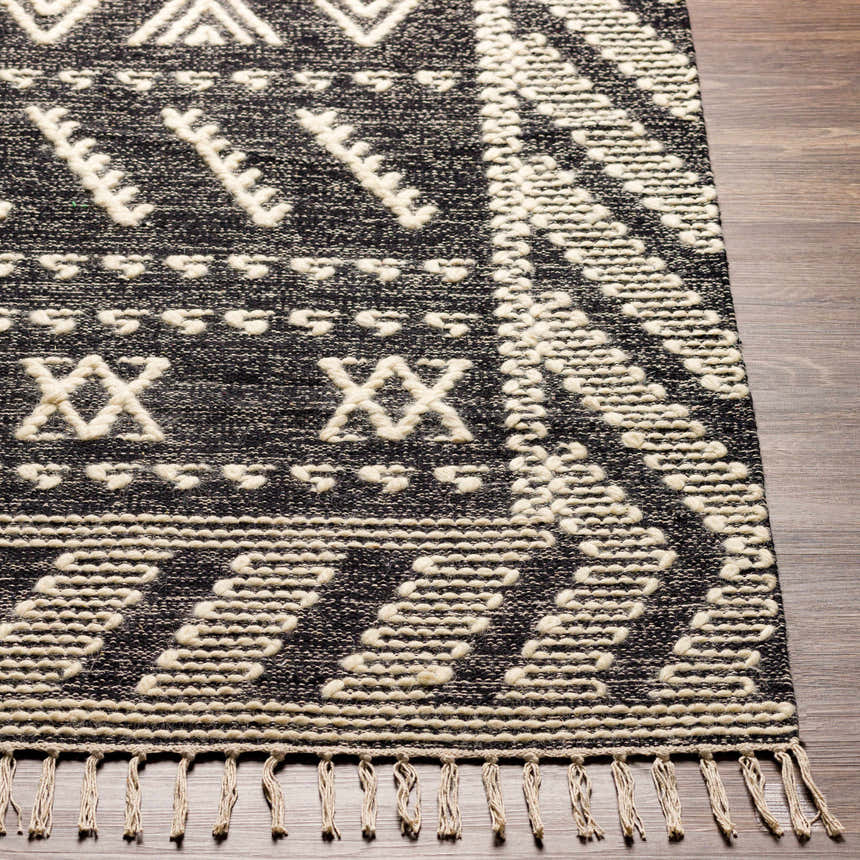 Close-up of the hand woven Rossville Area Rug. Black rug with geometric ivory pattern and tassels. Front