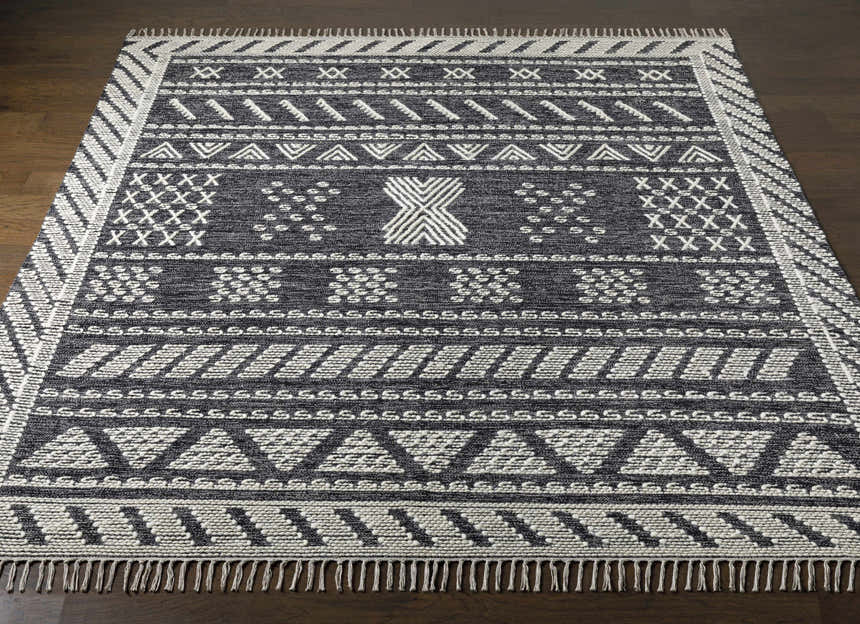 Hand woven Rossville Area Rug on dark wood floor. Features a black and white geometric design with fringe. Front